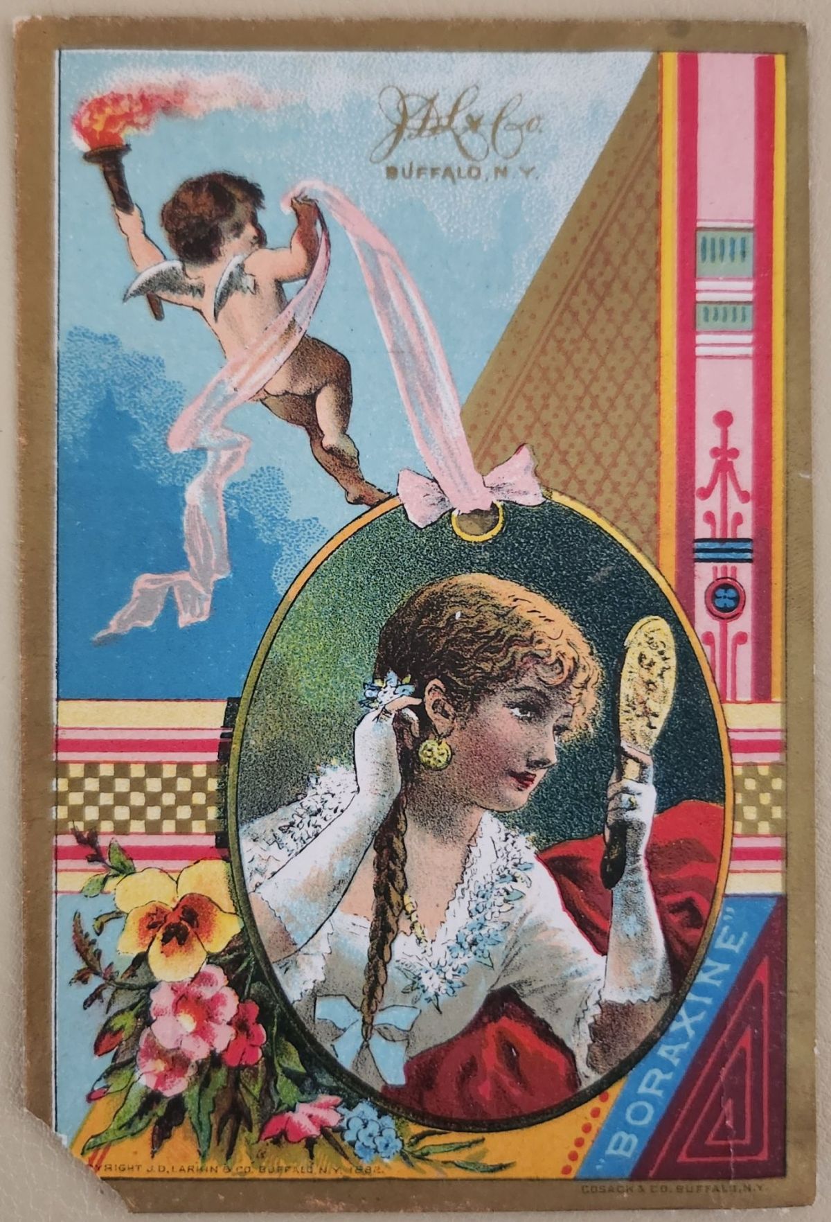 Victorian chromolithograph trade card showing a young woman with braided hair holding a hand mirror, wearing white lace and red fabric. A winged cherub flies upper left holding a flaming torch. Loose bouquet of pansies and forget-me-nots at lower left. Vertical Aesthetic Movement decorative panel at right. Round product medallion reads “Boraxine, Buffalo, N.Y.”